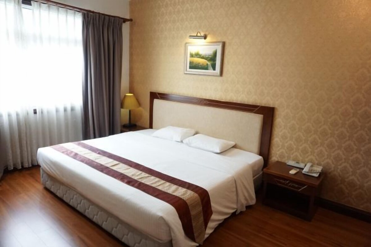 Una habitación de hotel con una cama grande, una mesita de noche con lámpara y un cuadro enmarcado en la pared.