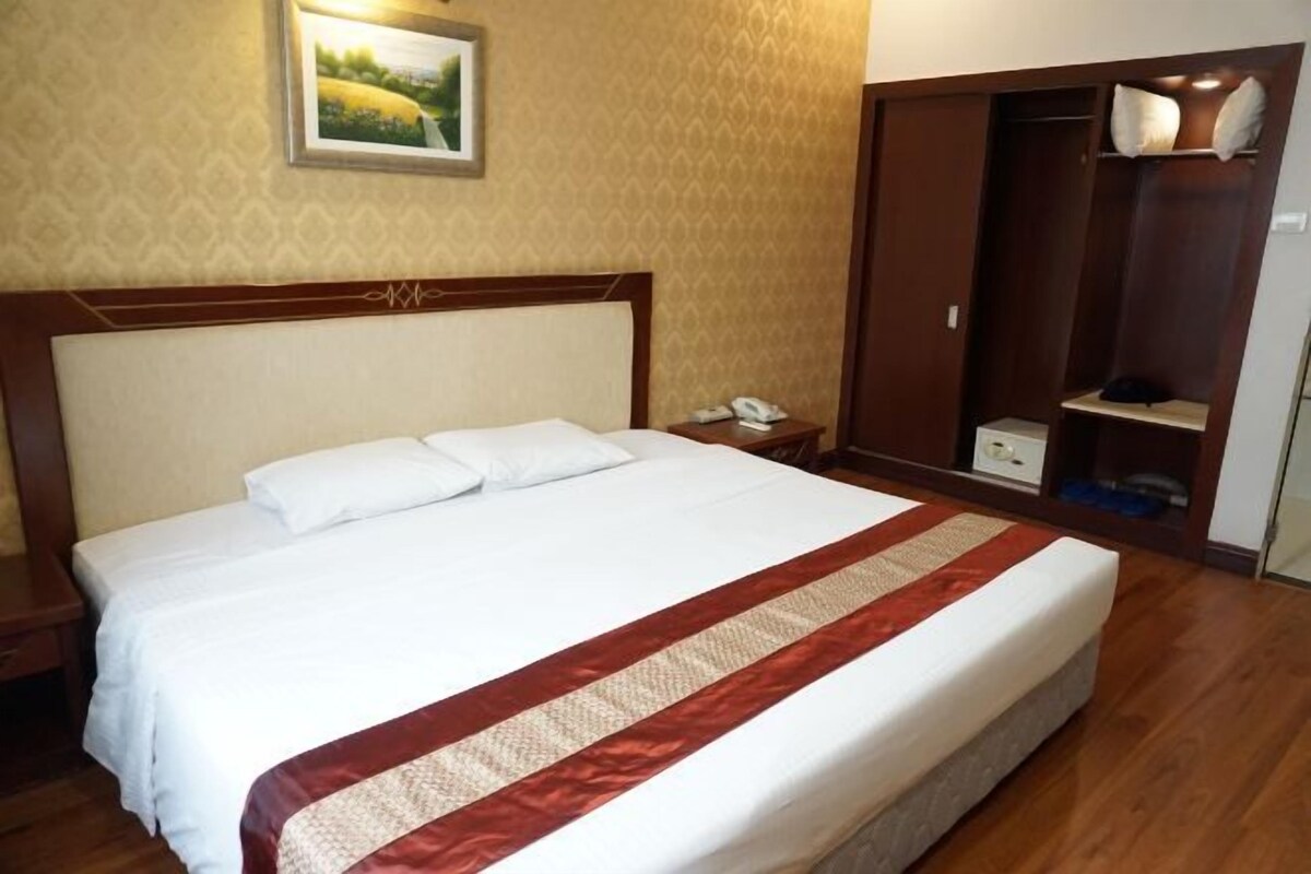 Een hotelkamer met een groot bed, een houten hoofdeinde, een nachtkastje, een telefoon, een kledingkast en een lijst aan de muur.