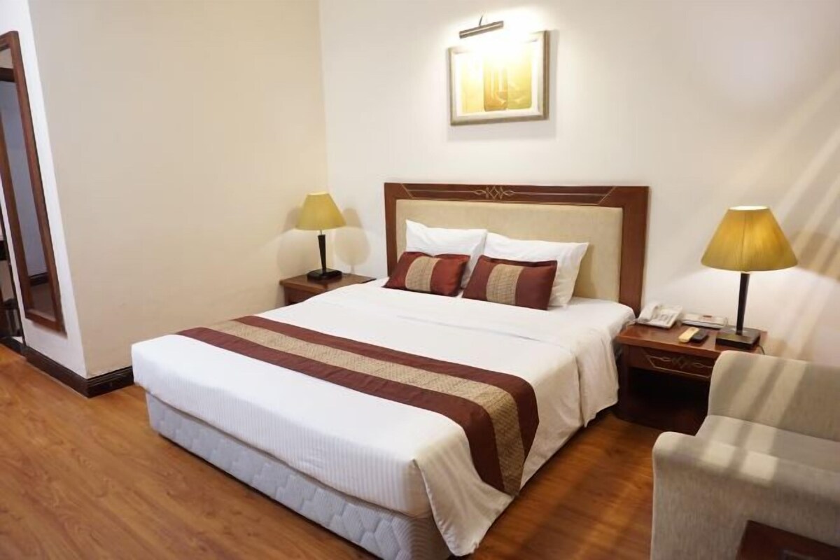 Een hotelkamer met een groot bed, twee nachtkastjes, een stoel en een wandlamp.