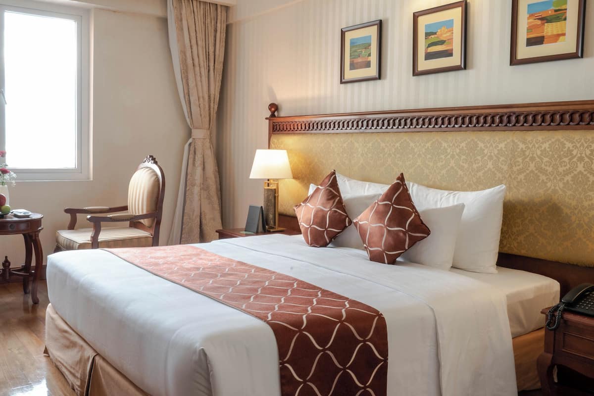 A hotel room with a large bed, a chair, a desk, and a lamp.