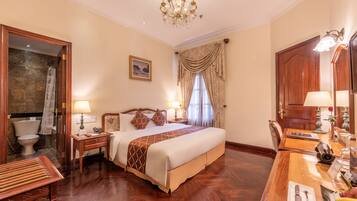 Une chambre d’hôtel avec un grand lit, un plancher en bois, un lustre et un bureau agrémenté d’un miroir et d’une lampe.