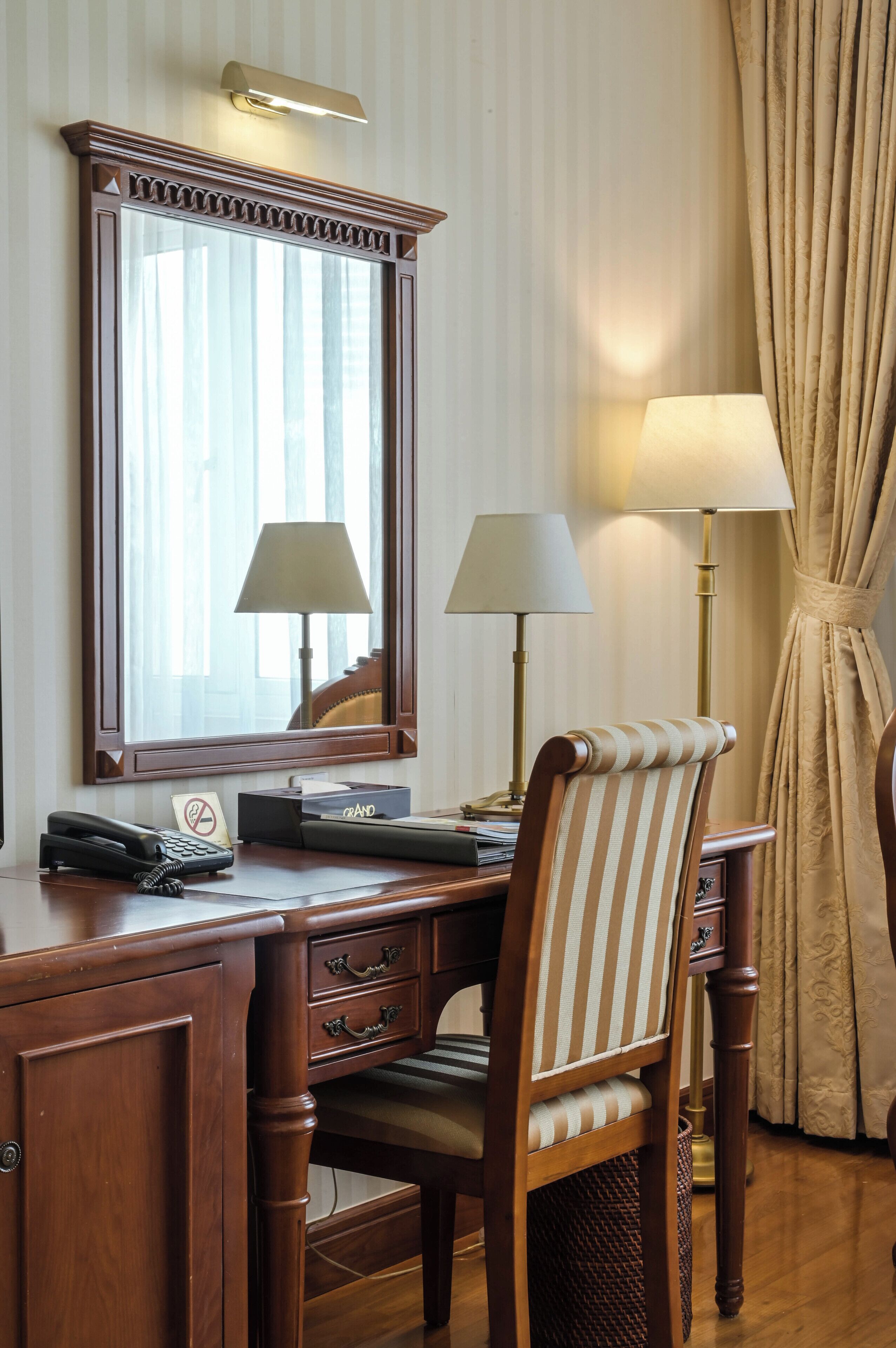 A wooden desk with a telephone, a lamp, and a chair with a striped cushion.
