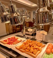 Ein reichhaltiges Buffet mit verschiedenen Speisen, darunter gebratenes Hähnchen und Speck auf Toast.