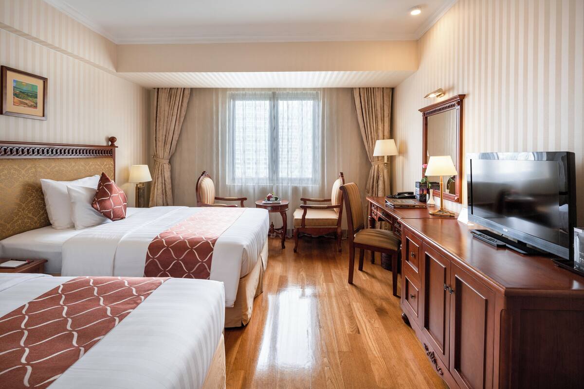 A hotel room with two beds, a desk with a TV, and a window with curtains.