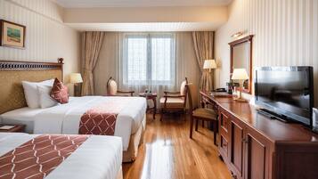 A hotel room with two beds, a desk with a TV, and a window with curtains.