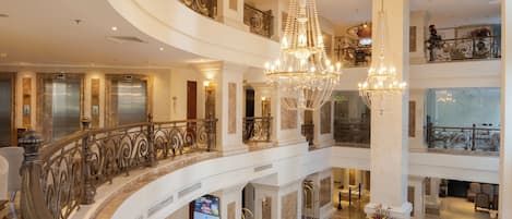 Un hall d’hôtel à plusieurs niveaux, doté d’un magnifique escalier, de lustres et d’un sol en marbre.