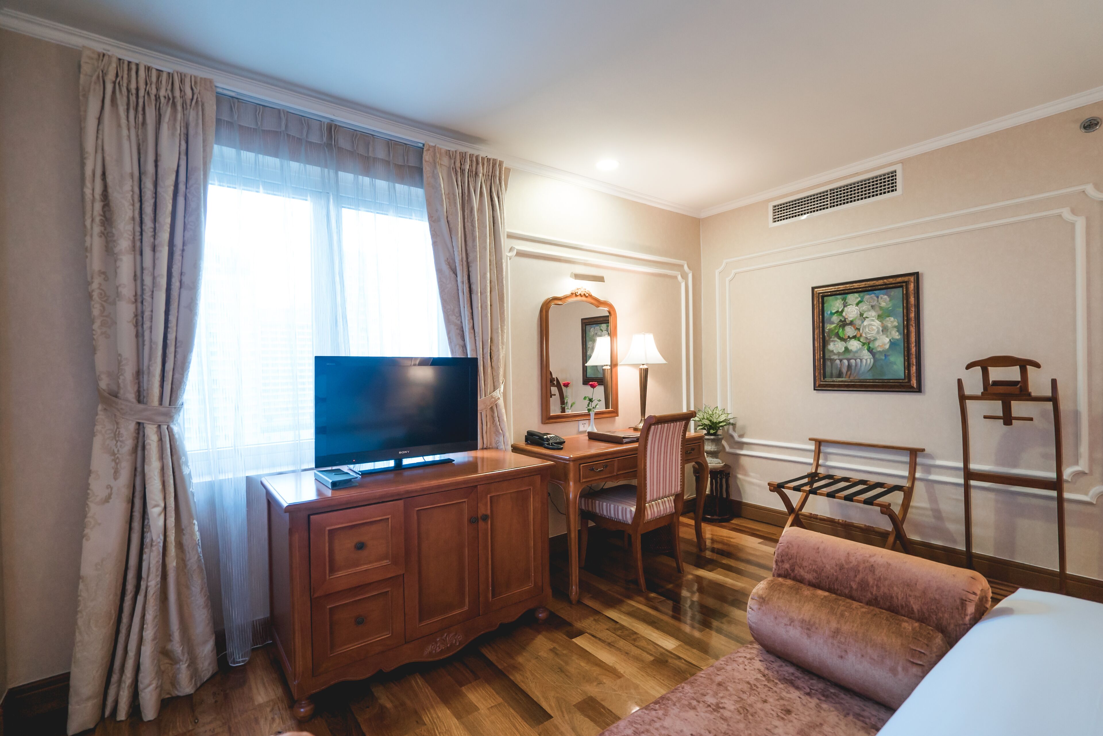 A hotel room with a wooden desk, a television, a chair, a sofa, and a painting on the wall.