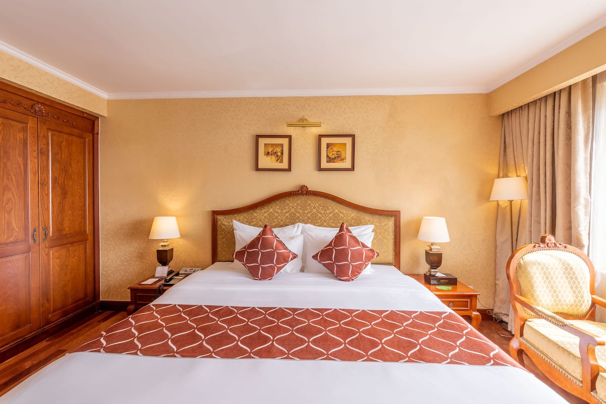 A hotel room with a large bed, two bedside lamps, a wooden wardrobe, and a chair.