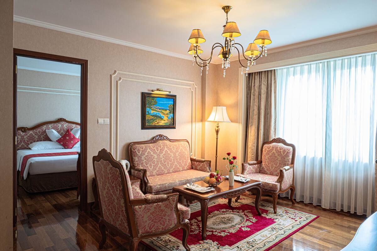 A hotel room with a bed, two armchairs, a coffee table, a lamp, and a large window with curtains.