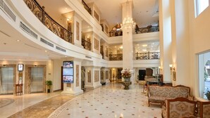 Un hall d’hôtel à plusieurs niveaux, doté de sols en marbre, d’un imposant lustre et de balustrades décorées.