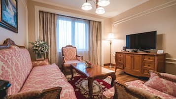 A room with a sofa, a chair, a wooden table, a television, and a lamp.