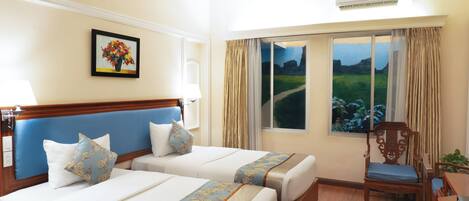 A hotel room with two beds, a window with a view of a landscape, a painting on the wall, and an air conditioning unit.