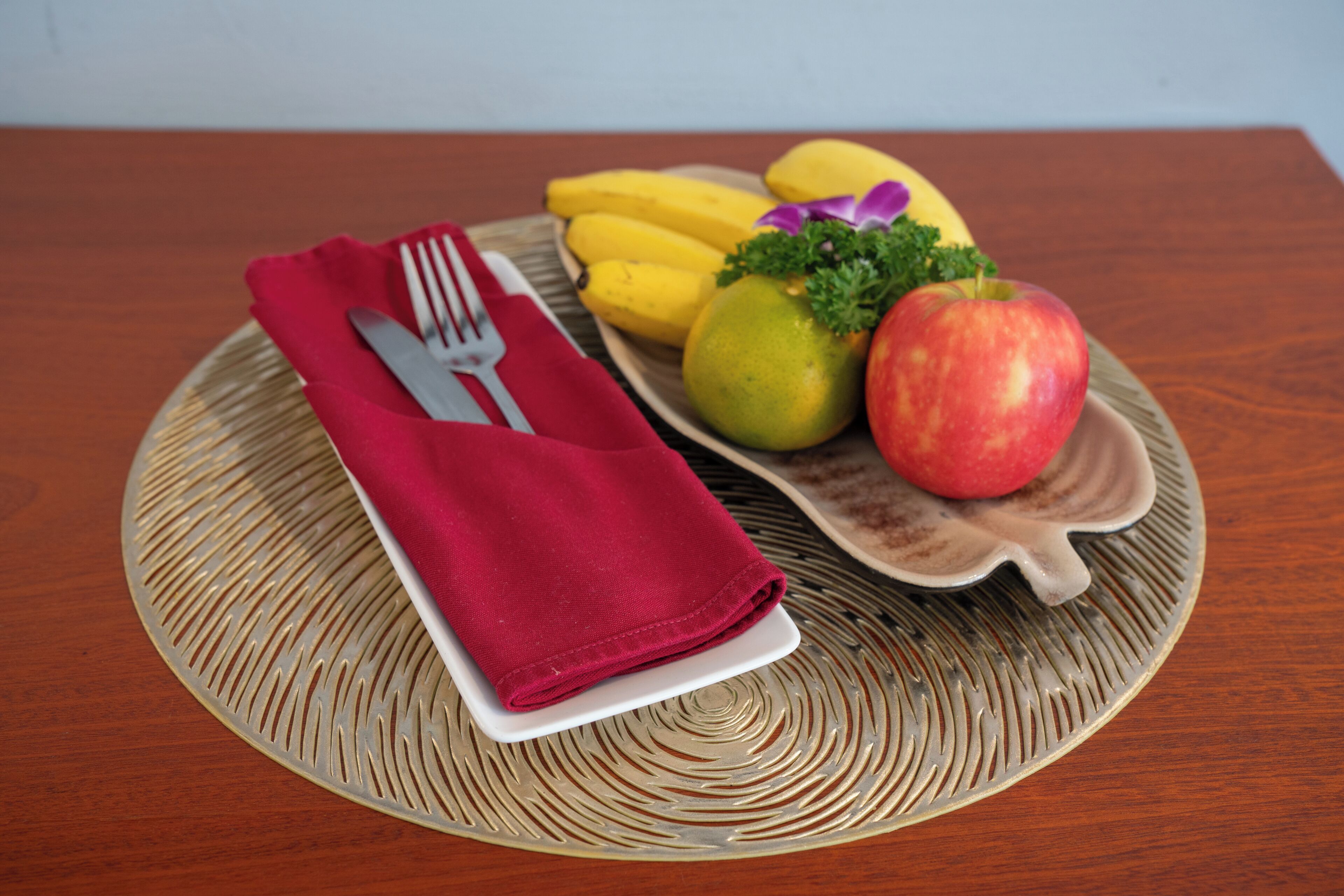 Une assiette avec une serviette pliée, une fourchette et un couteau, le tout posé sur un set de table texturé.