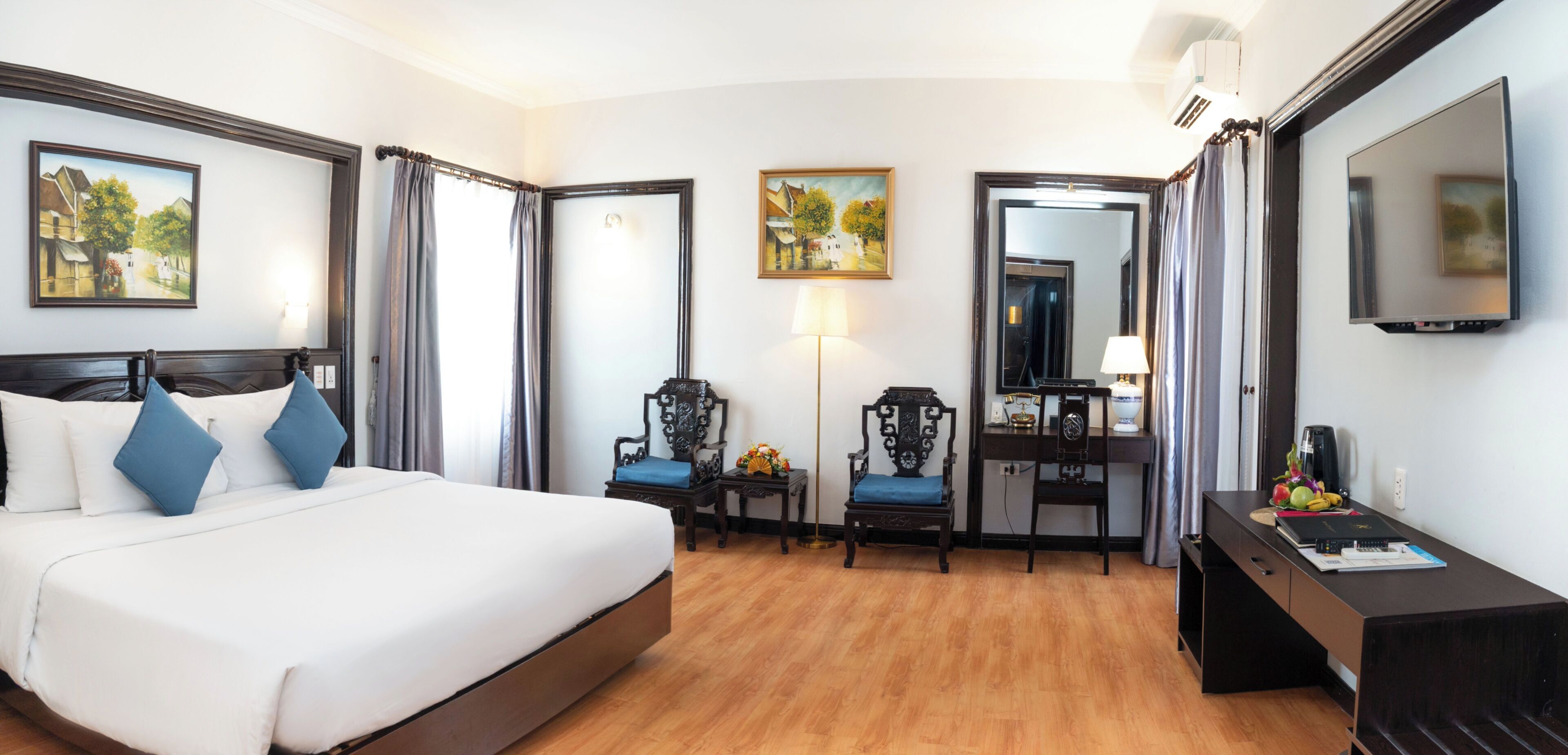 Ein Hotelzimmer mit einem großen Bett, zwei Stühlen, einem Schreibtisch, einem Spiegel und Bildern an den Wänden.