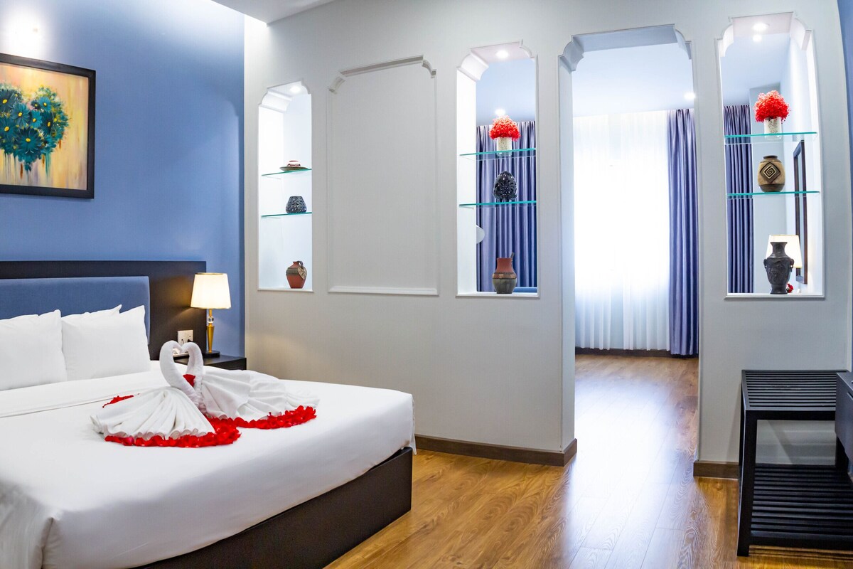 A hotel room with a large bed, bedside lamps, a painting on the wall, and a TV stand.