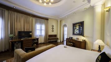 Ruime hotelkamer met groot bed, televisie, bureau met lamp en schilderij aan de muur.