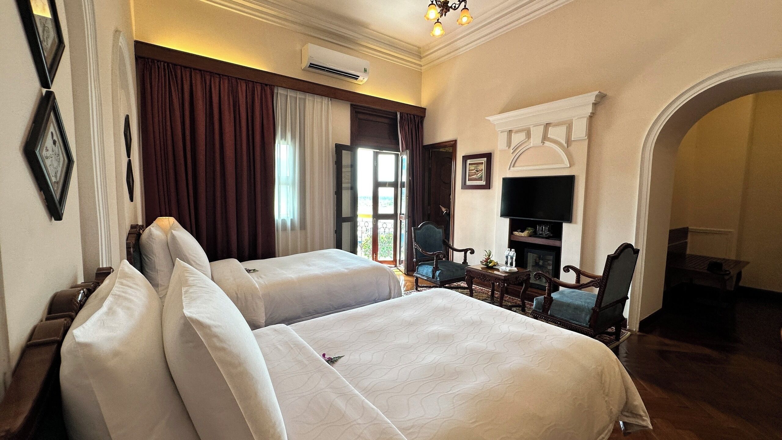 A hotel room with two beds, a television, a fireplace, and a dining area.