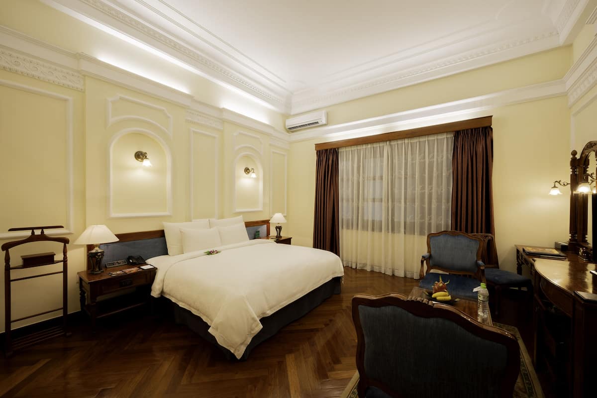 Ein Hotelzimmer mit einem großen Bett, Nachttischlampen, einem Schreibtisch mit Stuhl und einem Esstisch mit Stühlen.