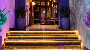 Een moderne hotellobby met een geometrisch plafondontwerp, een trap naar de verdieping erboven en een receptiezone met sfeerverlichting.