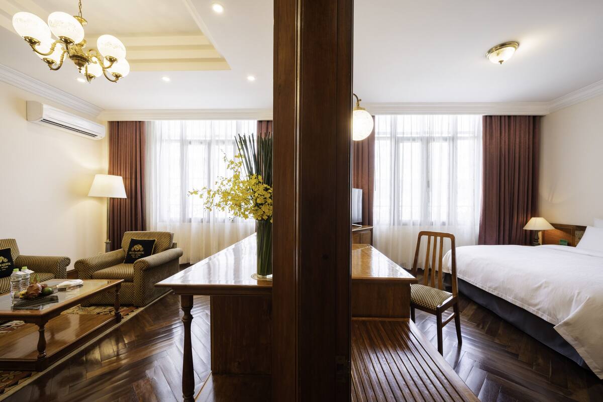 Ein Hotelzimmer mit Holzboden, einem Bett, einem Schreibtisch mit Stuhl, einer Couch und einem Blumenstrauß.
