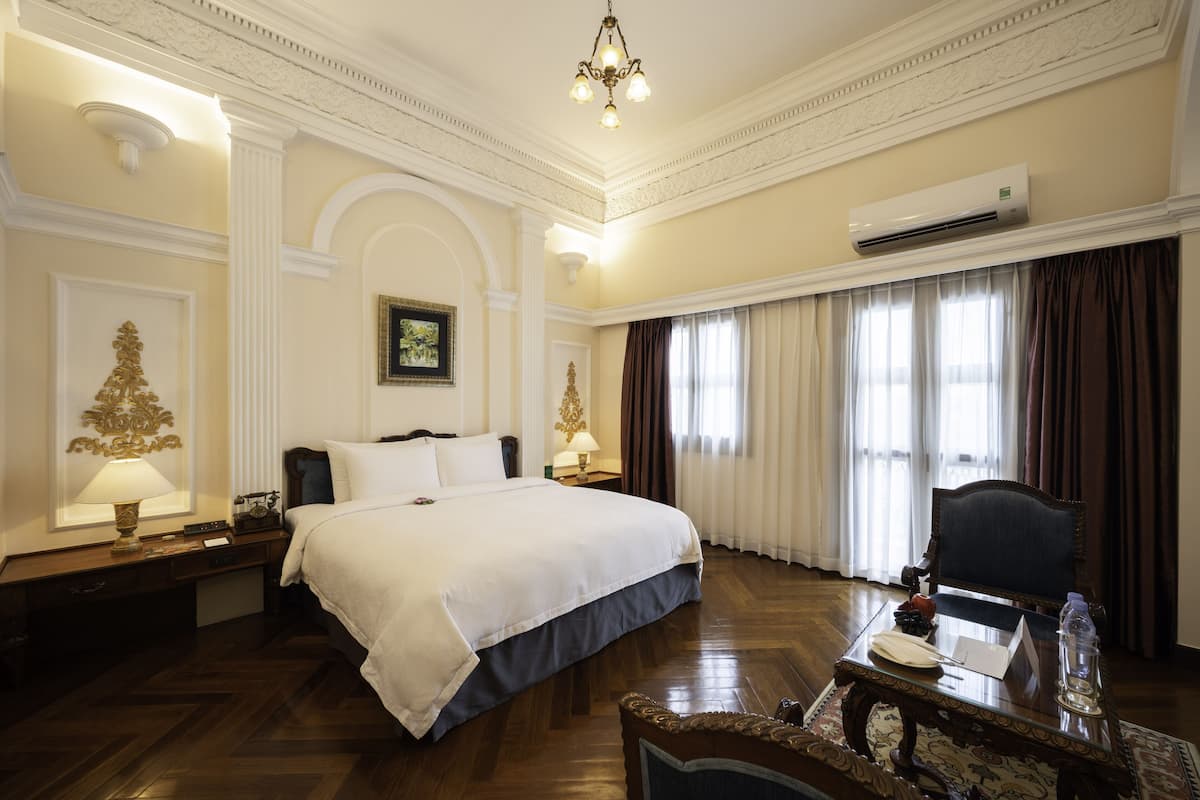 Ein Hotelzimmer mit einem großen Bett, einem Schreibtisch mit Stuhl, einer Klimaanlage und einem Chandelier.