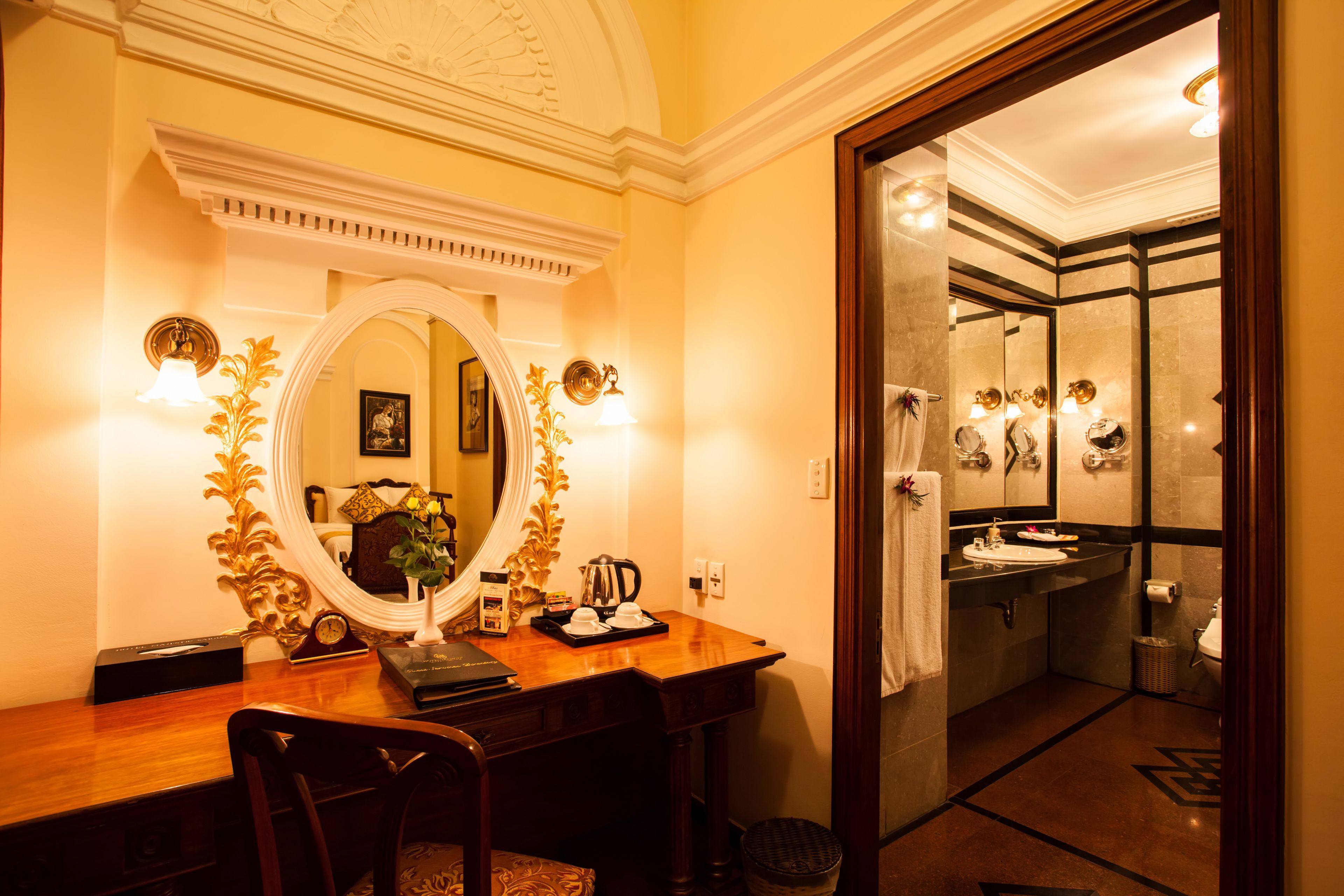 A hotel room with a wooden desk, a large mirror, and a bathroom visible through an open door.