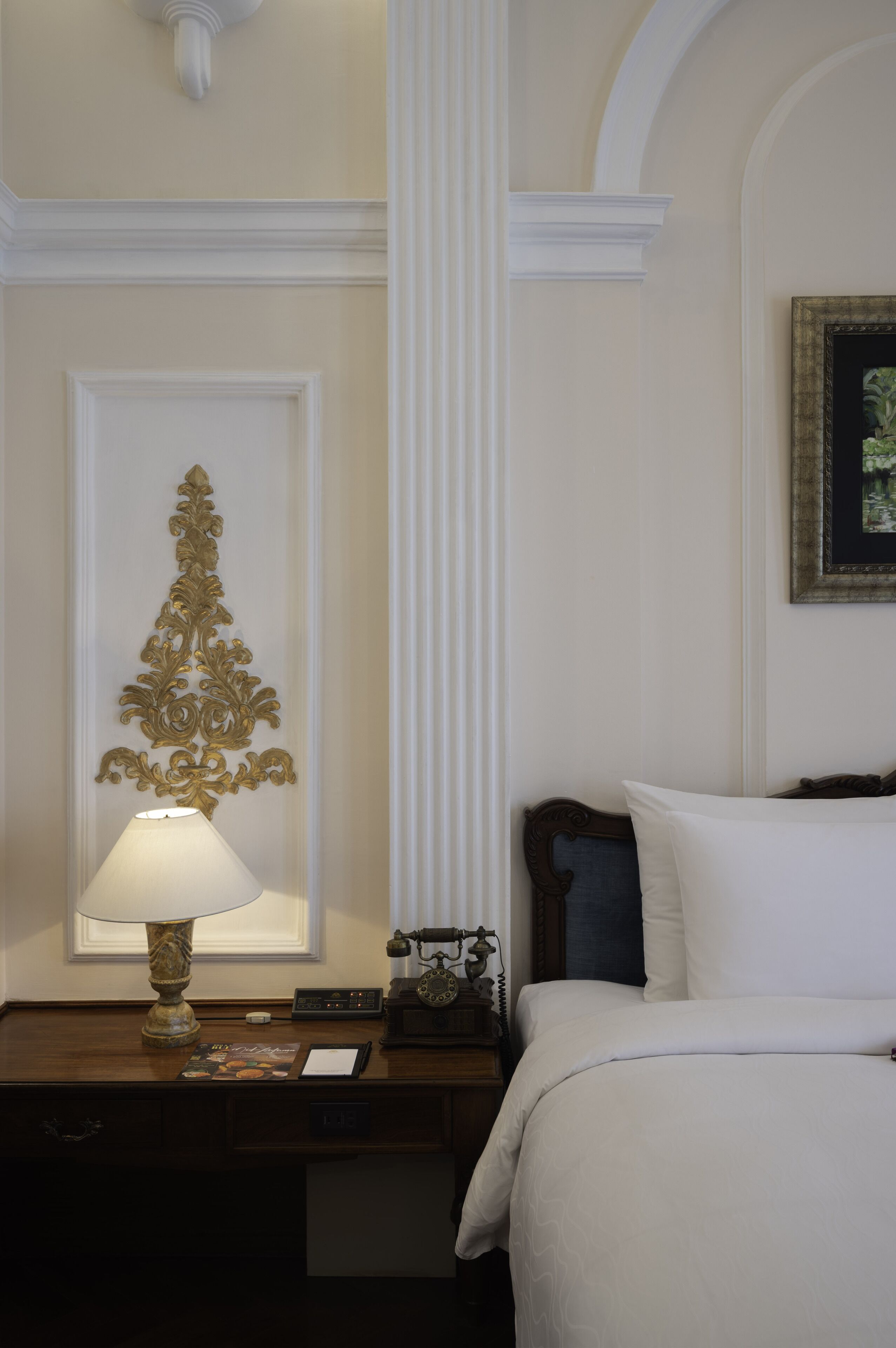 Una habitación de hotel con una cama, una mesita de noche con una lámpara, un adorno en la pared y un cuadro enmarcado.