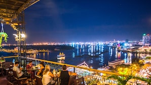Een restaurant aan het water met terras, uitzicht op een rivier, stadslichten op de achtergrond en een panorama van de skyline.