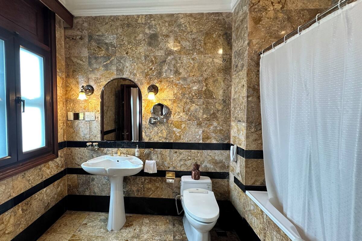 Ein Badezimmer mit Marmorwand, Waschbecken, Toilette und Duschvorhang.