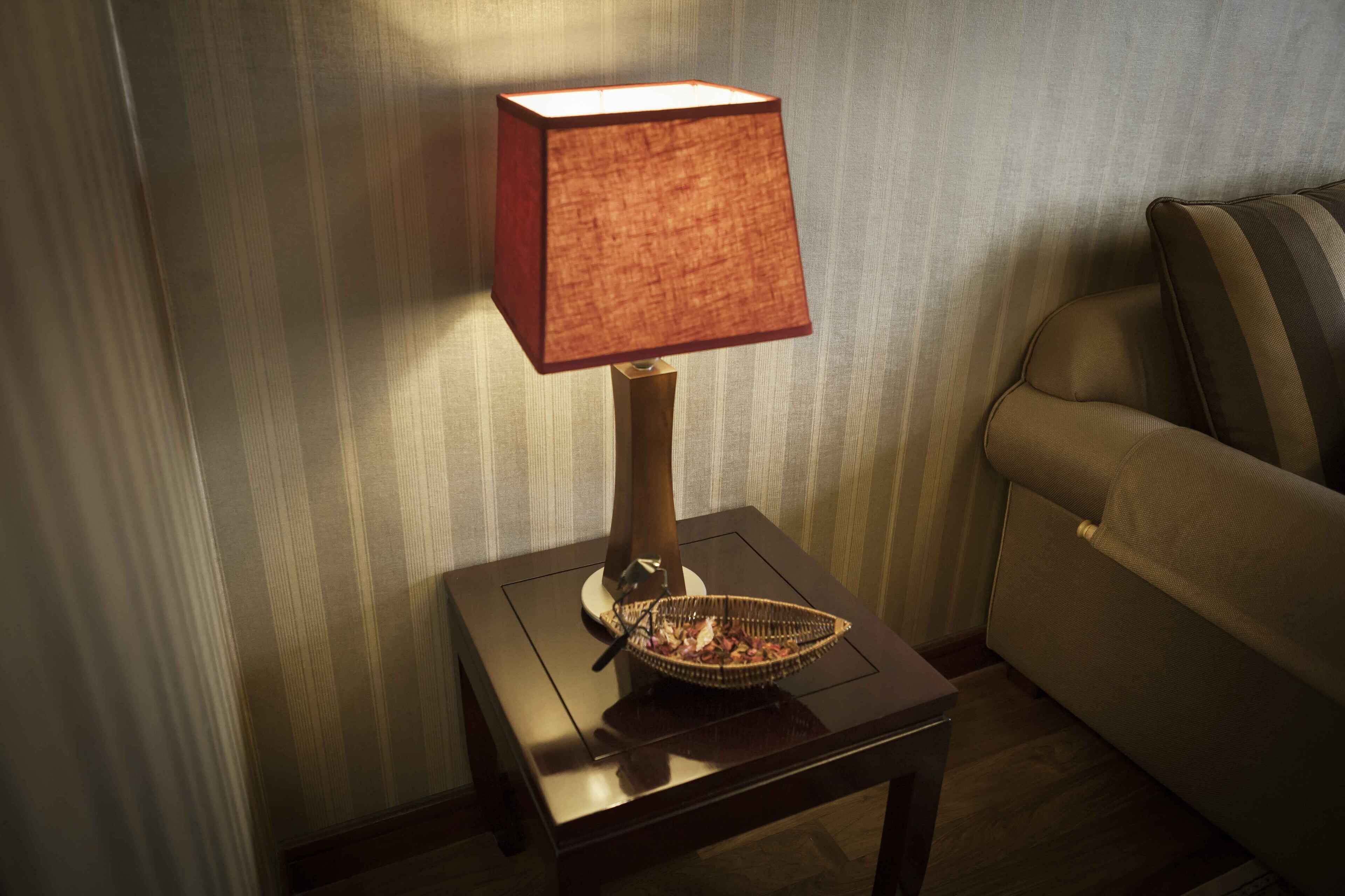 A lamp on a small table with a basket on it, next to a sofa.