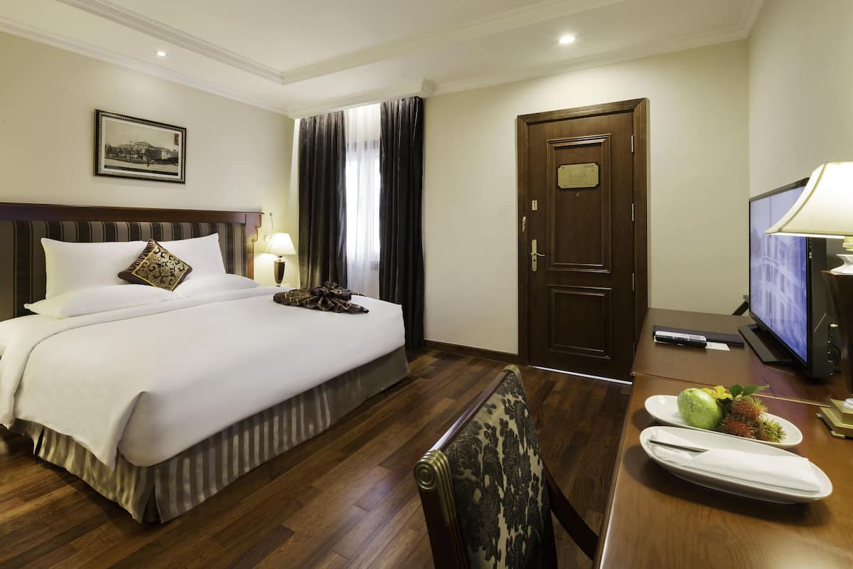 Ein Hotelzimmer mit einem großen Bett, einem Holztisch, einem Fernseher und einer Tür.