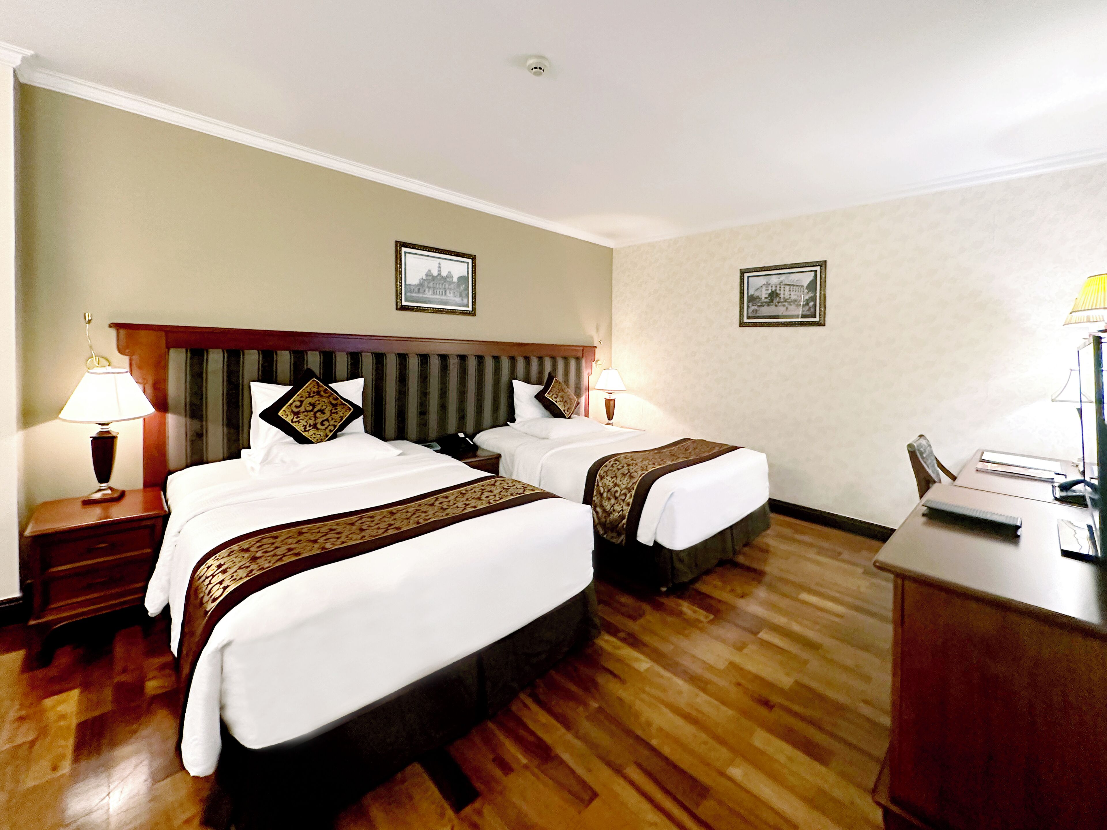 A hotel room with two beds, wooden headboards, and a desk with a chair.