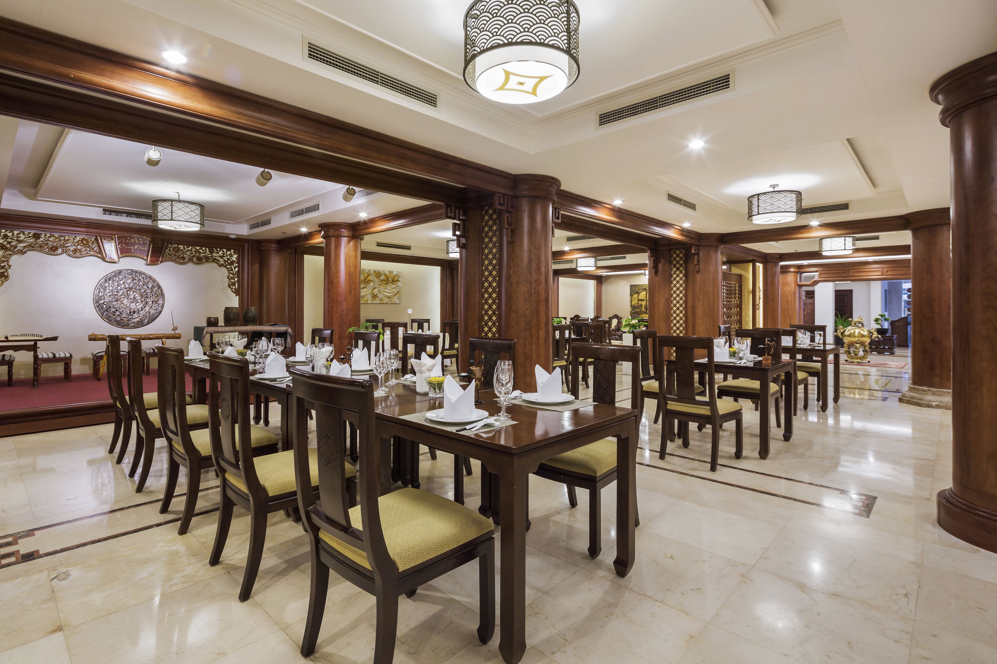 A spacious dining area with wooden tables and chairs, a decorative wall, and a chandelier.