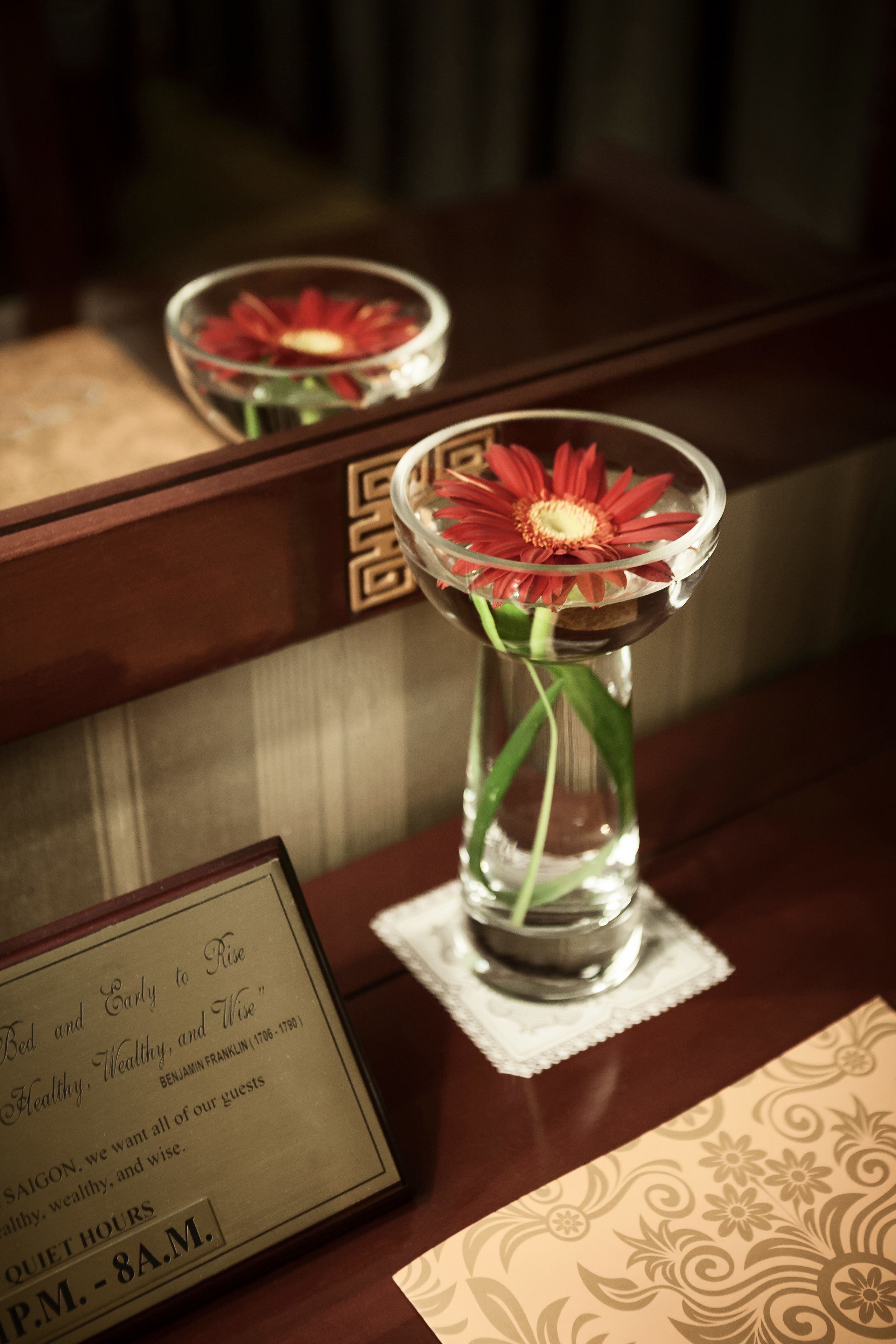 A framed sign with a message and a vase with a red flower on a wooden surface.