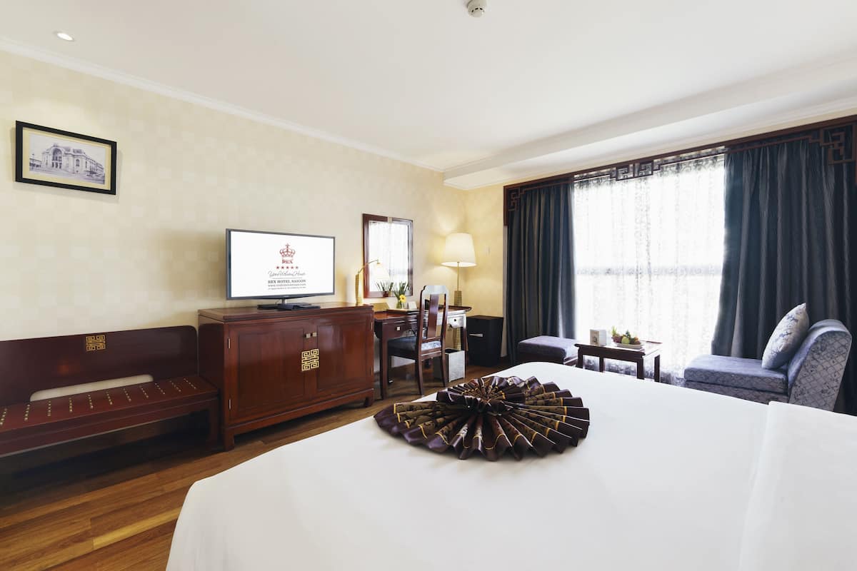 Ein Hotelzimmer mit Bett, Schreibtisch, Stuhl, Fernseher und einem Fenster mit Vorhängen.