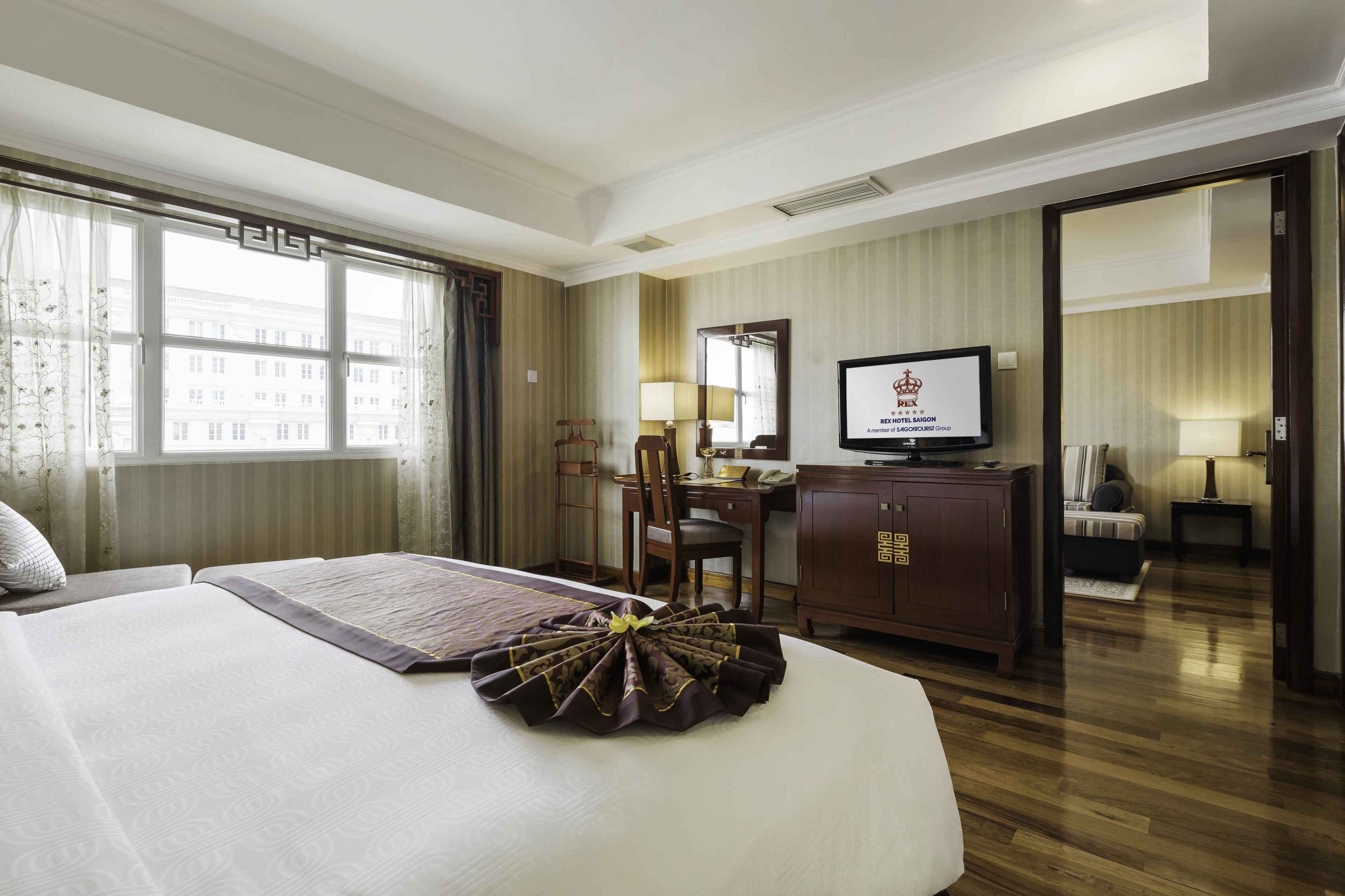 A hotel room with a large bed, a desk with a computer, a television, and a view of buildings outside.