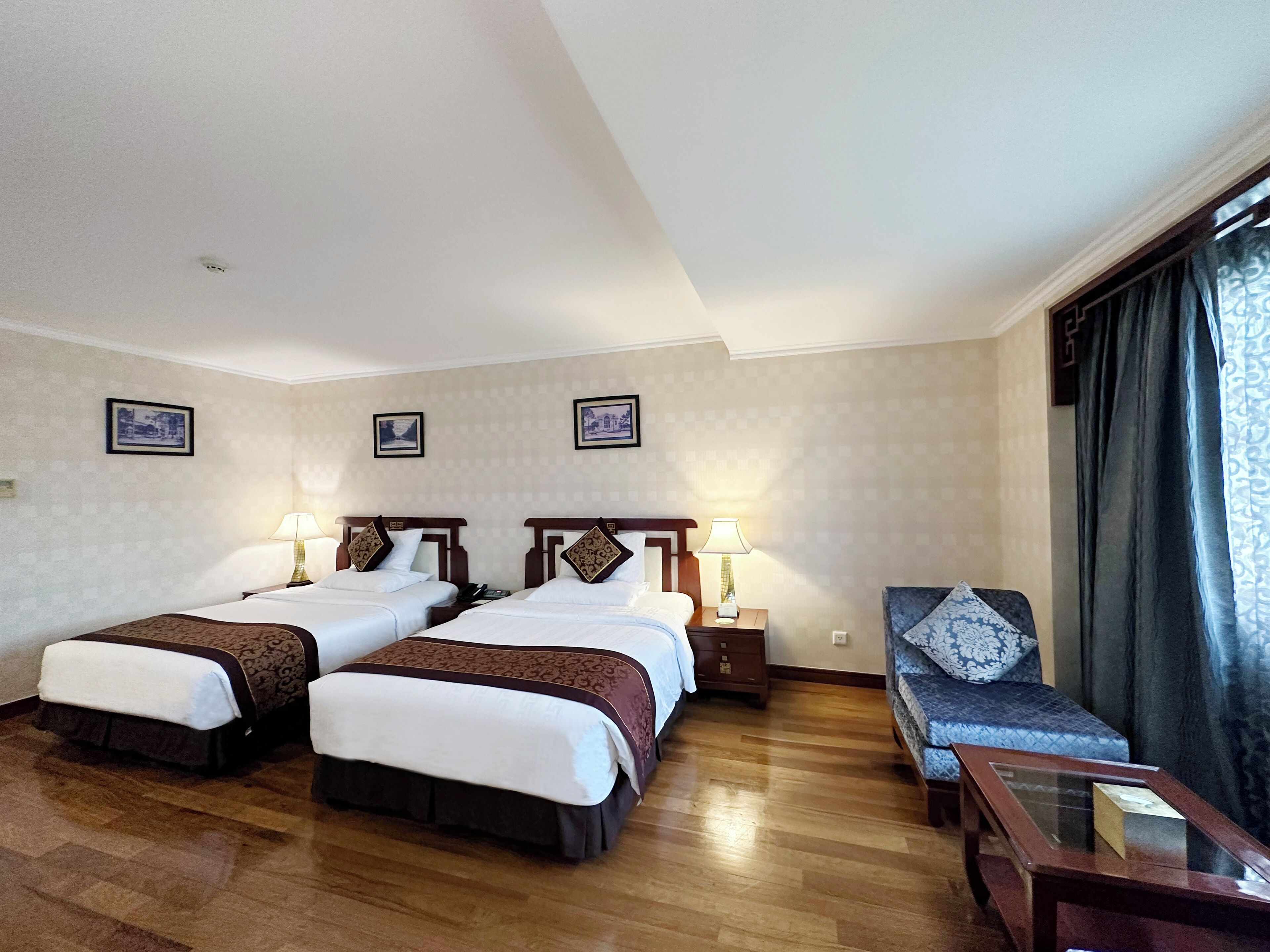 A hotel room with two beds, a sofa, a small table, and a window with curtains.