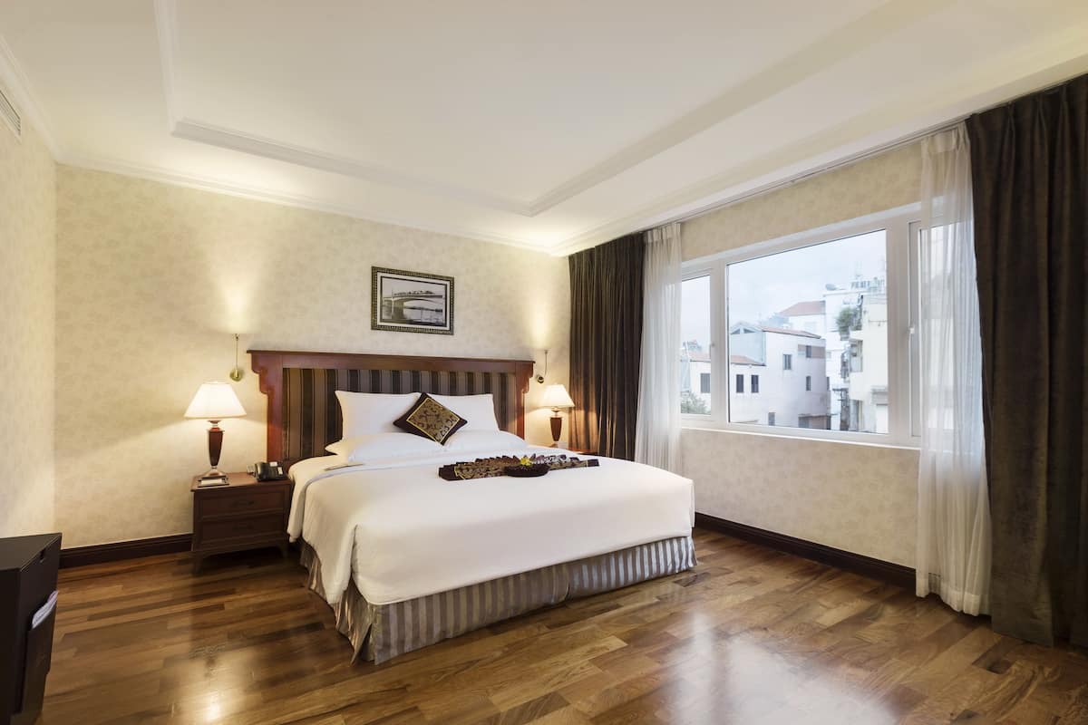 Ein Hotelzimmer mit einem großen Bett, zwei Nachttischen mit Lampen, einem gerahmten Bild an der Wand und einem Fenster mit Vorhängen.