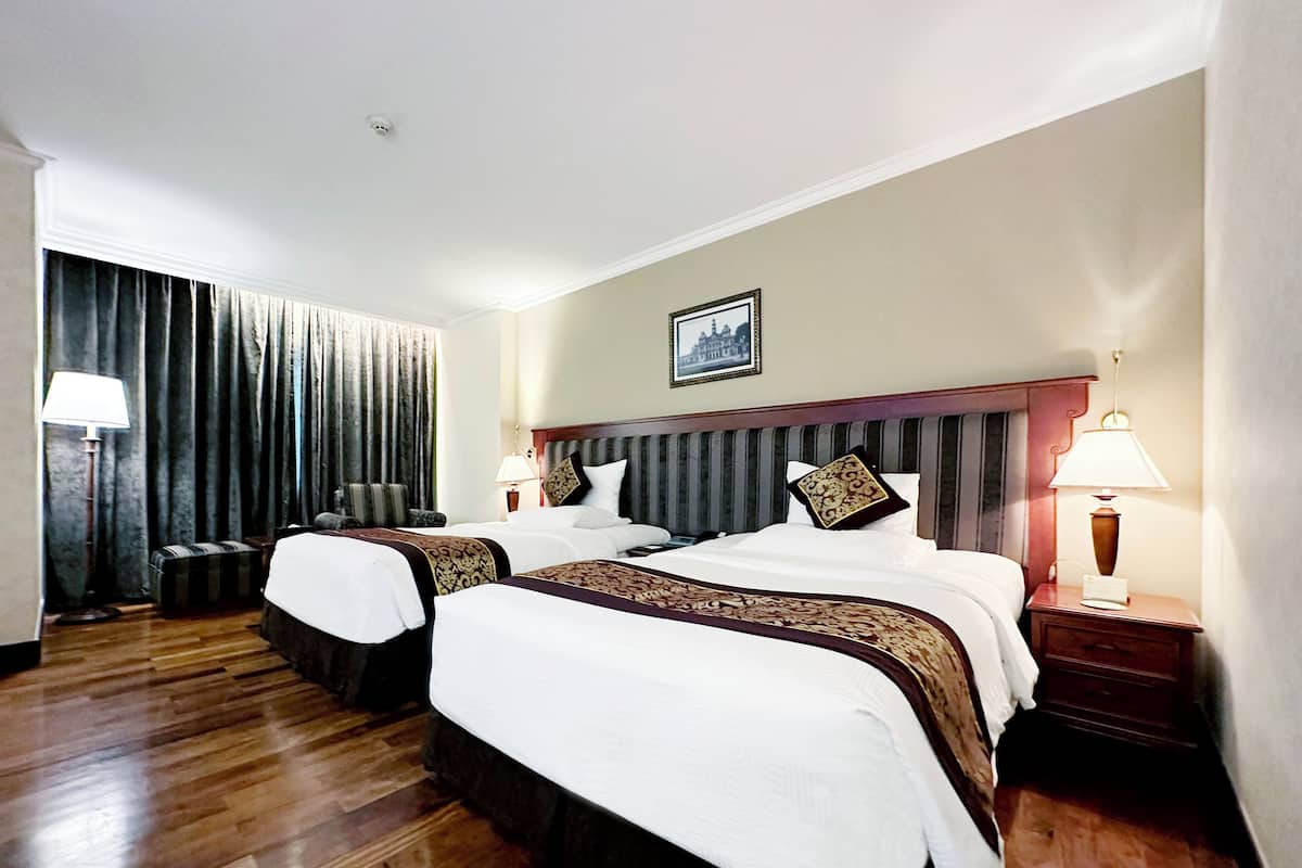 Ein Hotelzimmer mit zwei Betten, einem großen Fenster mit Vorhängen, Holzboden und einem gerahmten Bild an der Wand.