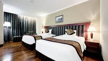 A hotel room with two beds, a large window with curtains, a wooden floor, and a framed picture on the wall.