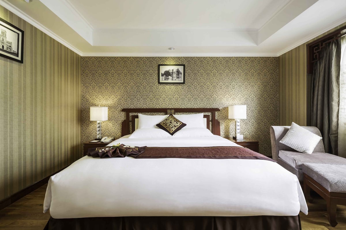 Ein Hotelzimmer mit einem großen Bett, zwei Nachttischen, einem Sessel und einem Bild an der Wand.
