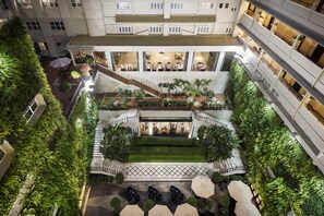 A multi-level hotel atrium with a central staircase, outdoor seating, and lush greenery. - Rex Hotel (Ho Chi Minh City)
