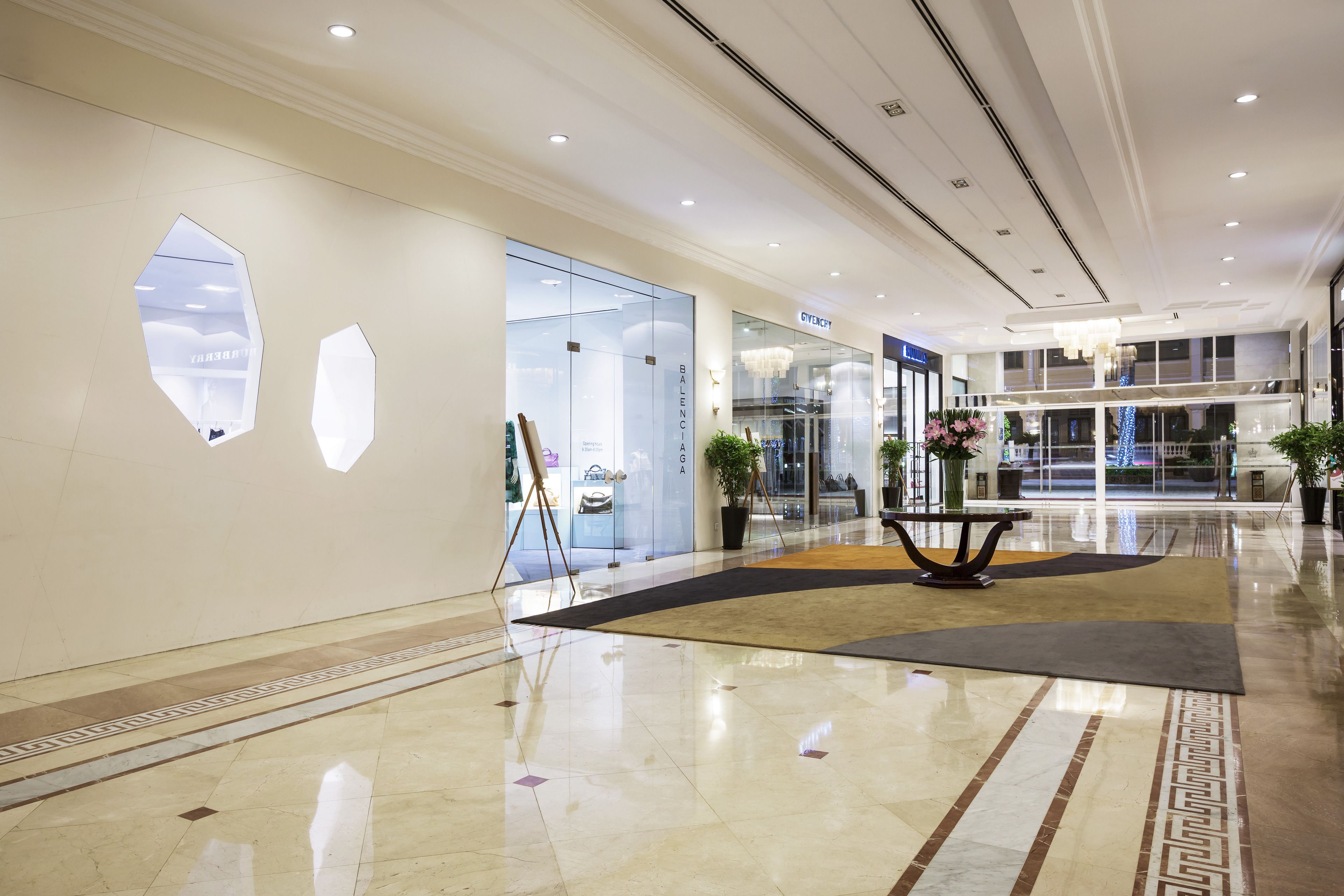 A modern hotel lobby with a polished marble floor, a central seating area, and a glass storefront.