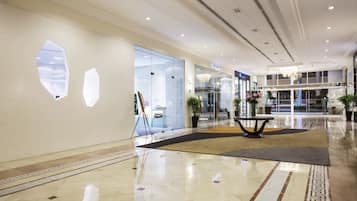 A modern hotel lobby with a polished marble floor, a central seating area, and a glass storefront.
