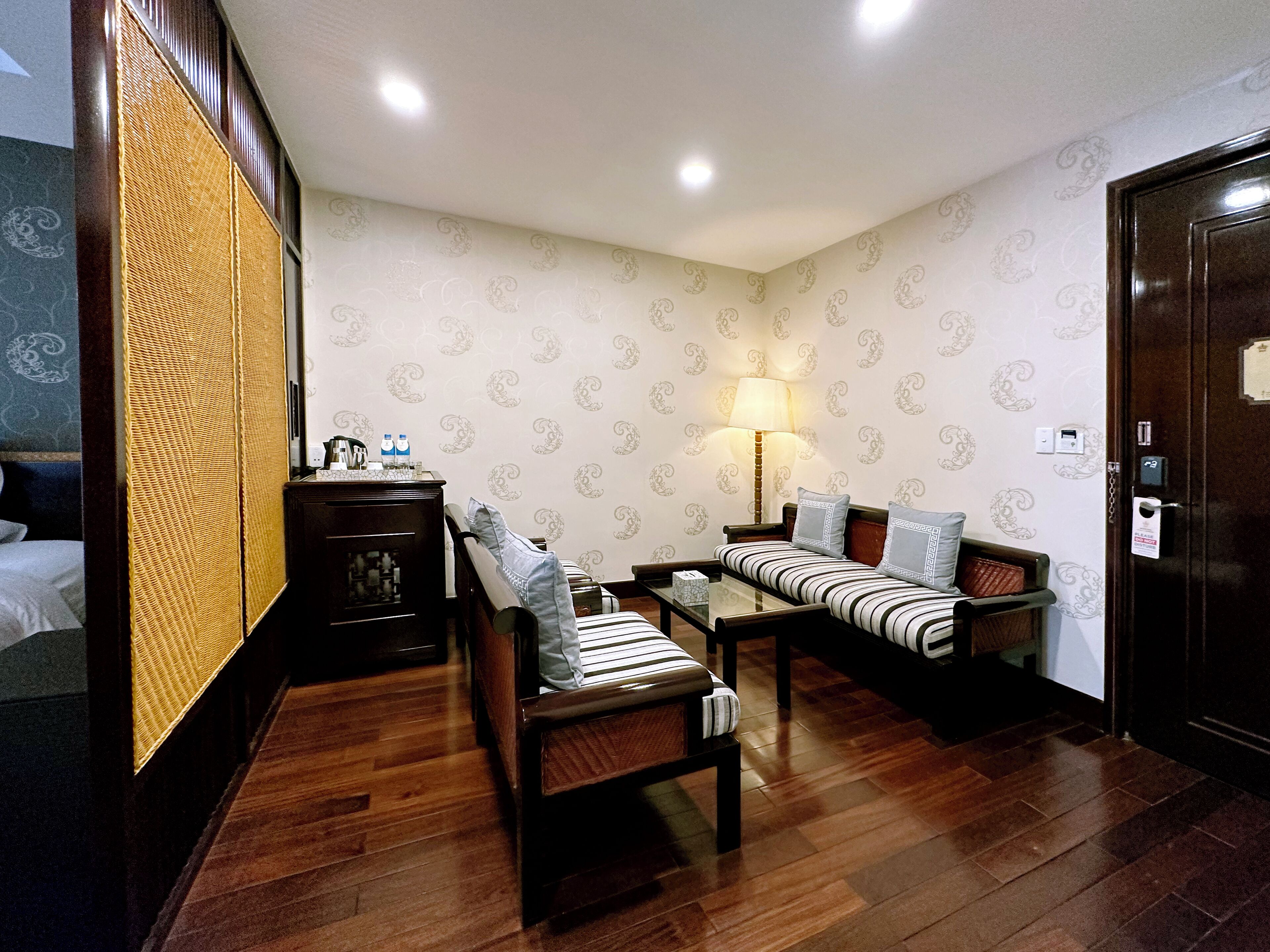 A hotel room with a bed, a sofa, a small table, a lamp, and a wooden wardrobe.
