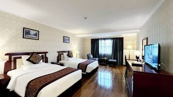 A hotel room with two beds, a desk, a television, and a window with curtains.