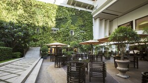 Un patio al aire libre con varias mesas y sillas, rodeado de abundante vegetación y un camino de piedra.