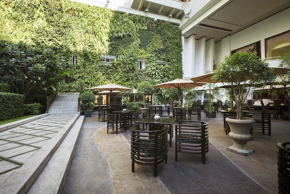 An outdoor patio area with multiple tables and chairs, surrounded by lush greenery and a stone pathway. - Rex Hotel (Ho Chi Minh City)