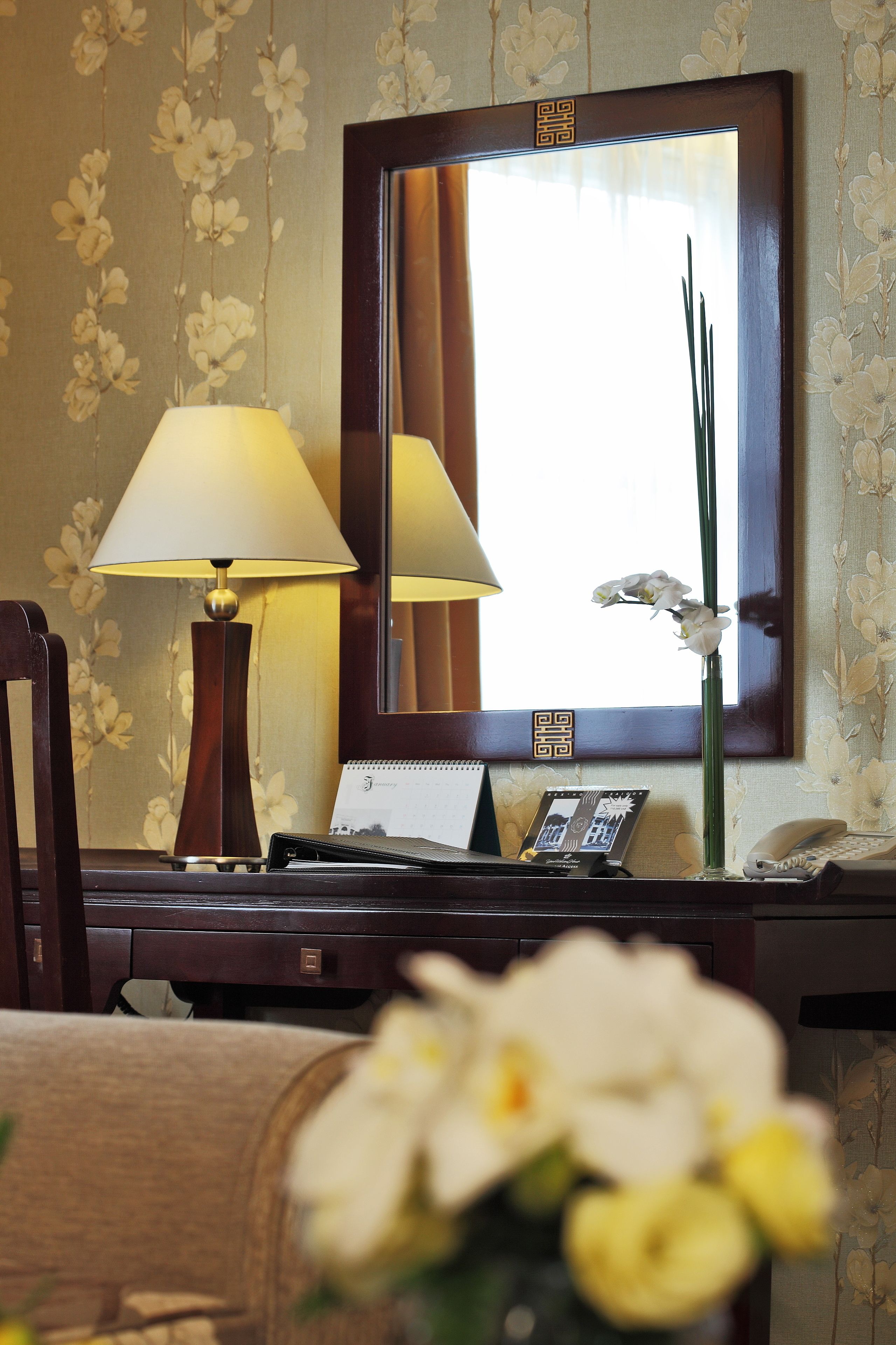 A hotel room with a desk, a lamp, a telephone, and a mirror.