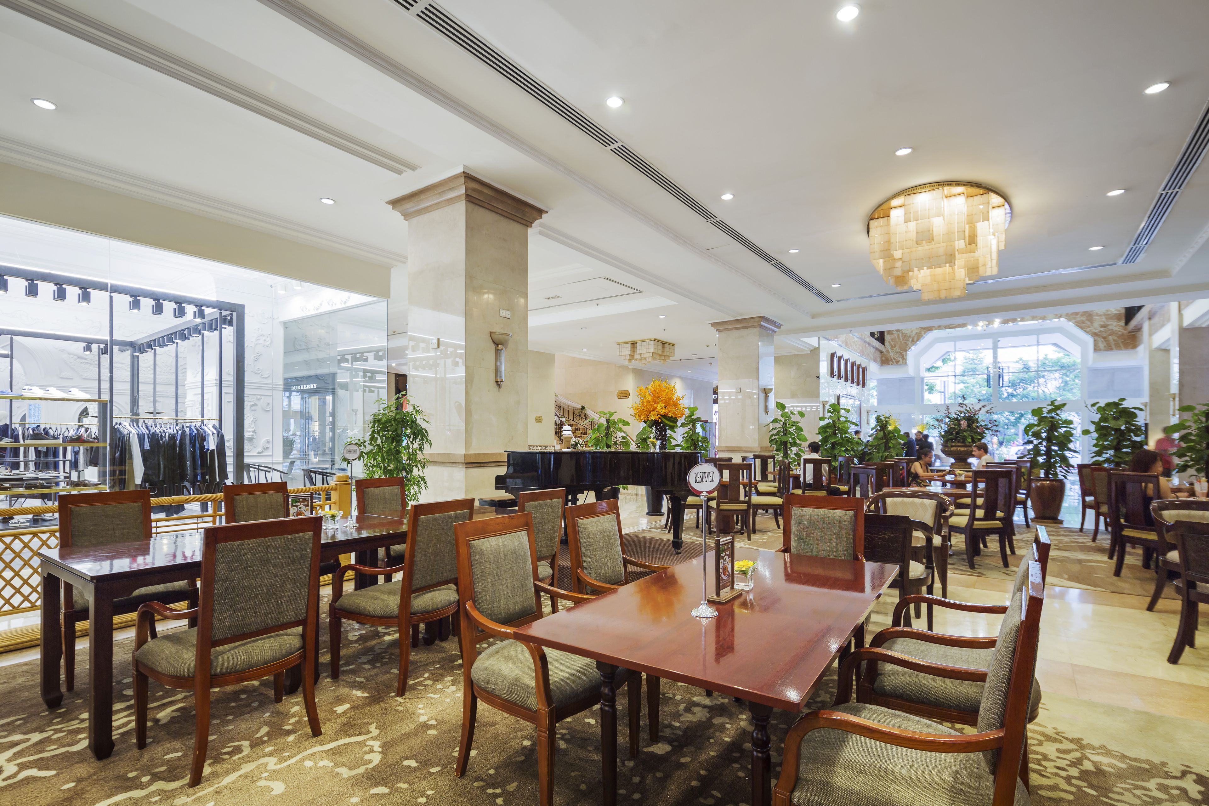 A spacious hotel lobby with a grand chandelier, multiple dining tables, and comfortable seating.